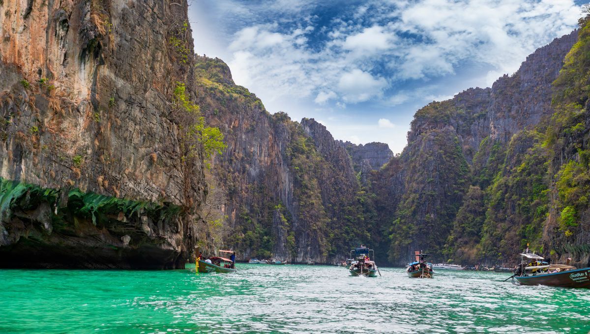 Longtail boats on bright turquoise water between steep limestone cliffs
