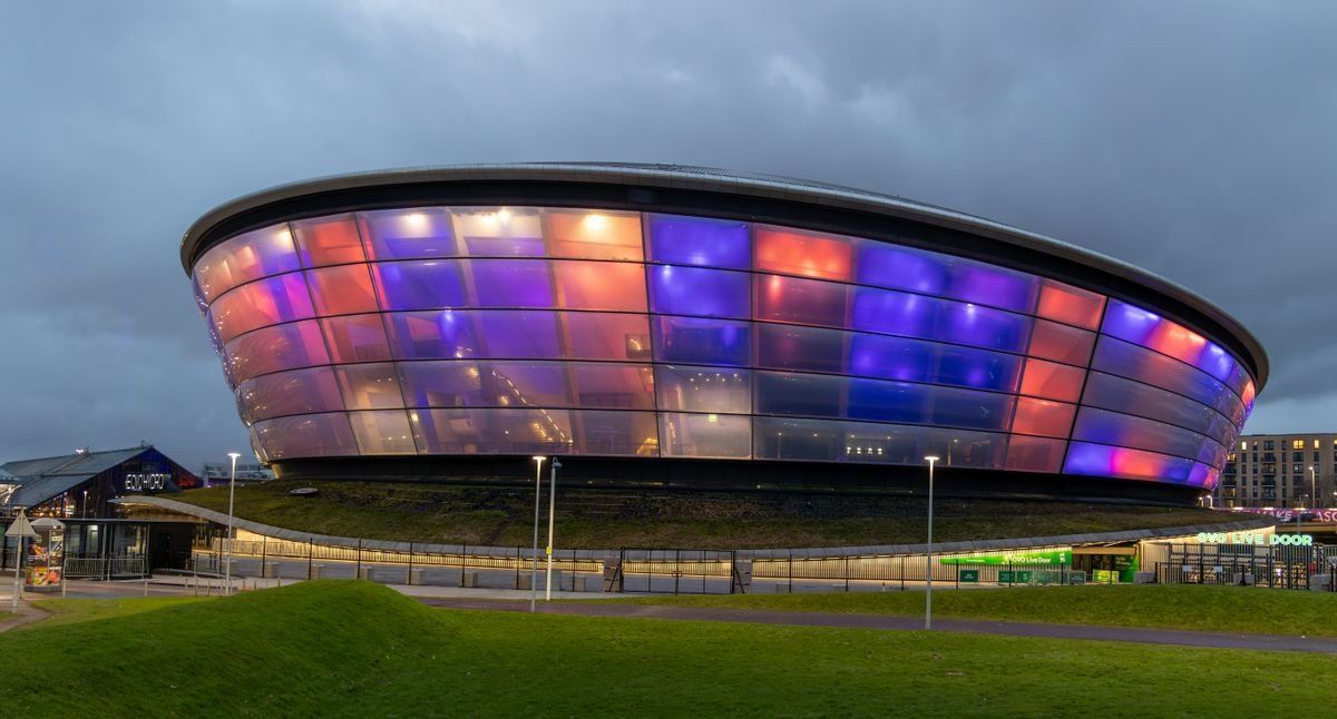 OVO Hydro at night glowing in purple, blue, and red lights above a grassy foreground