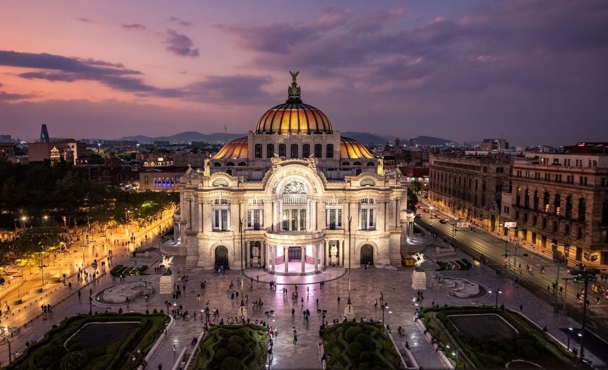 Palacio de Bellas Artes illuminated at sunset with people in the square and city streets around it
