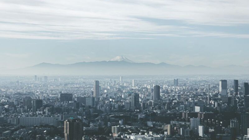 Panoramic view of Tokyo cityscape with Mount Fuji looming in the background, under cloudy skies. Panoramic view of Tokyo cityscape with Mount Fuji looming in the background, under cloudy skies.