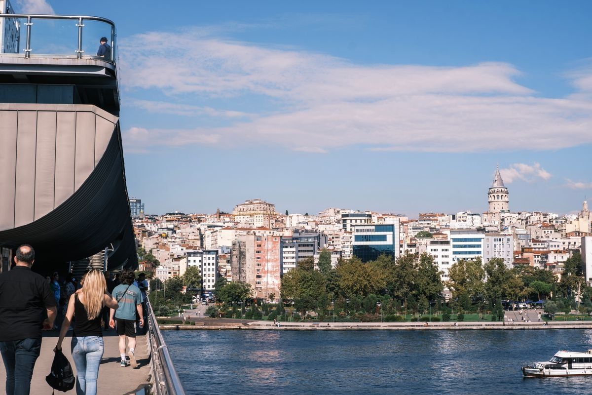 People walking along a bridge above the water with Istanbul skyline and Galata Tower in the distance