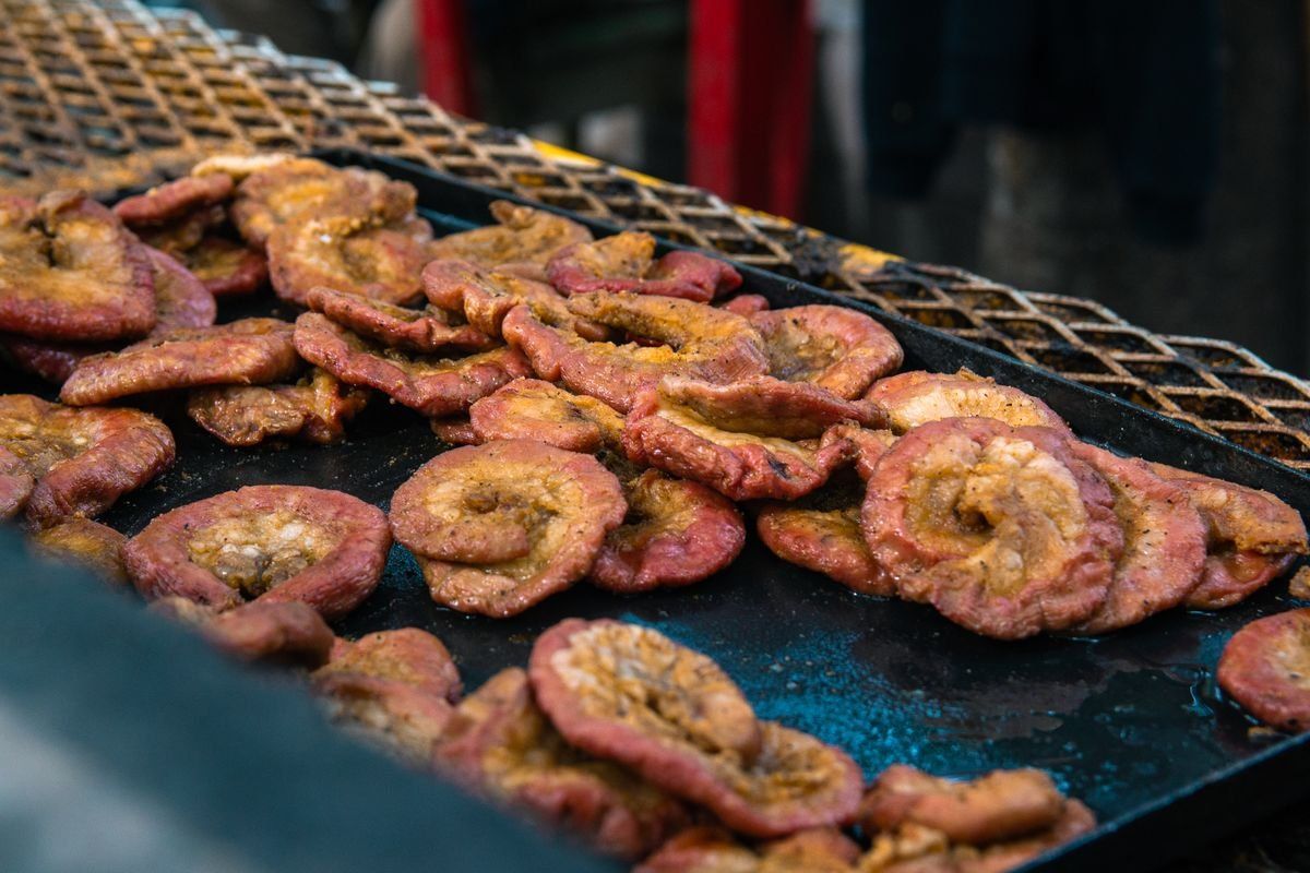 Ring-shaped pieces of meat grilling on a metal grate over an open flame