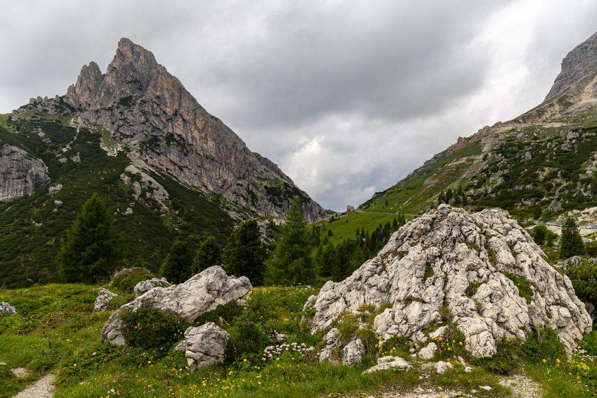 Rocky Dolomite peaks rising above green meadows and pale boulders under heavy clouds