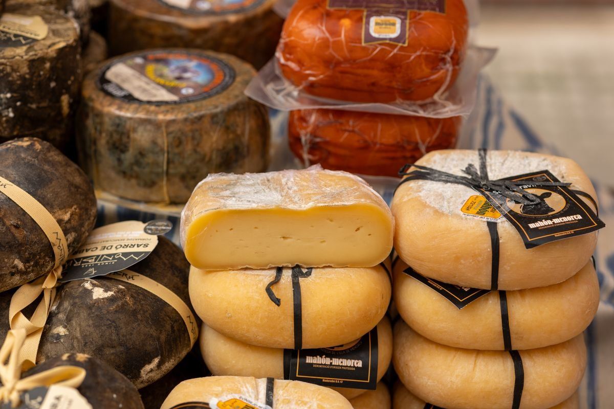 Rounds of aged and semi-soft cheese stacked on display at a market stall