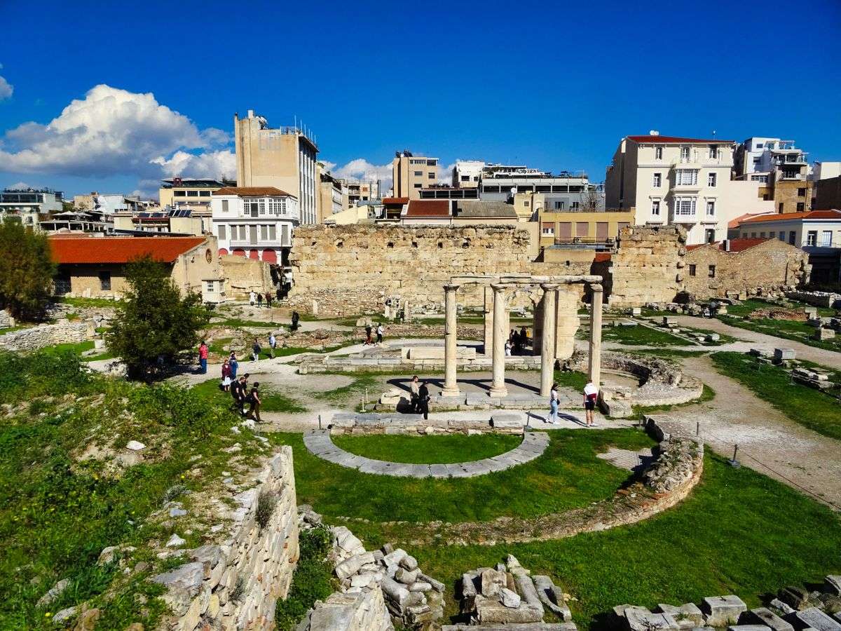 Ruins of Hadrian's Library with circular columns, grass, and surrounding city buildings
