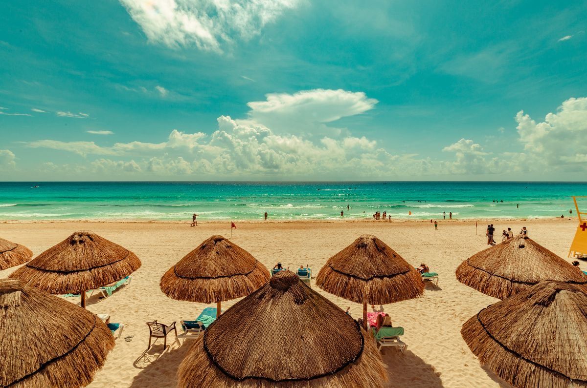Sandy beach with straw umbrellas and turquoise sea under a bright cloudy sky