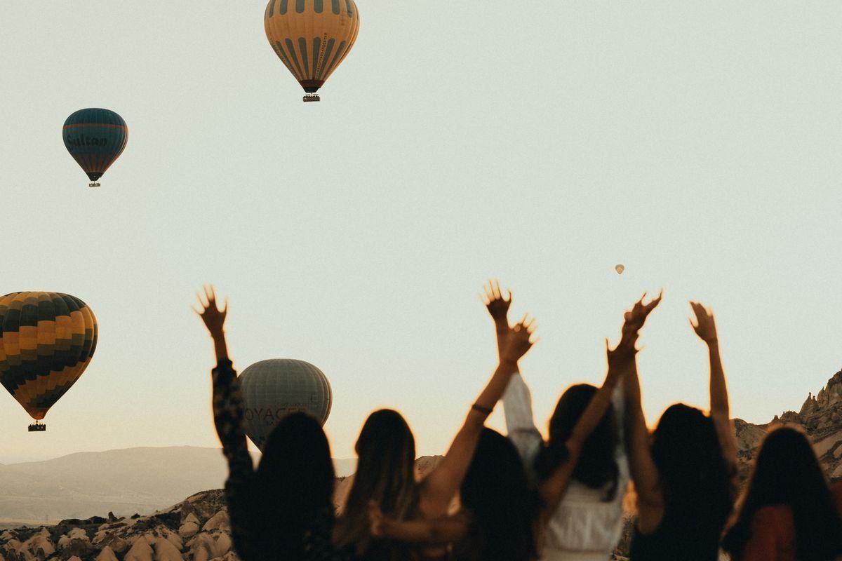 Silhouettes of women with raised arms watching hot air balloons in the evening sky
