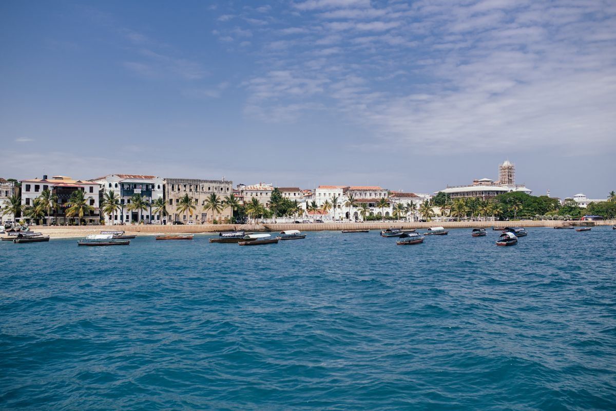 Small boats on blue water facing Stone Town waterfront under a lightly clouded sky