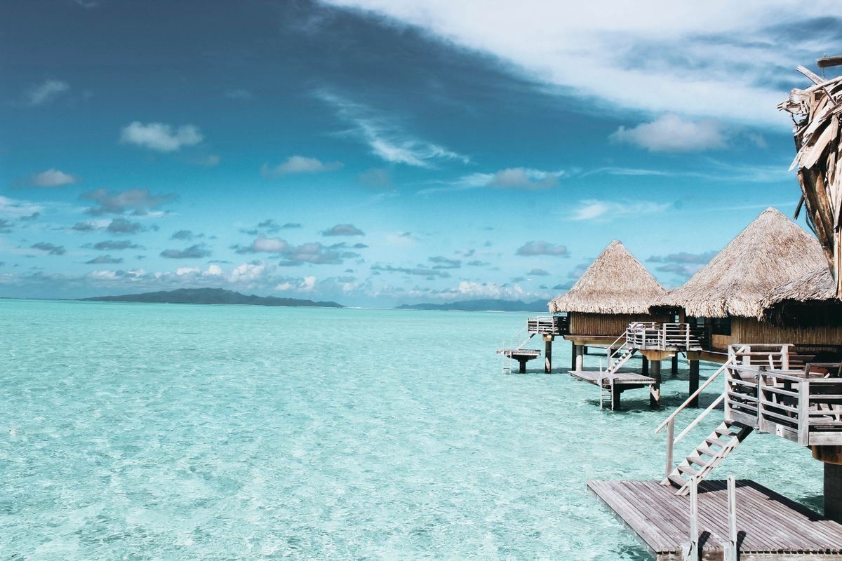Thatched overwater bungalows above shallow turquoise sea with distant islands on the horizon