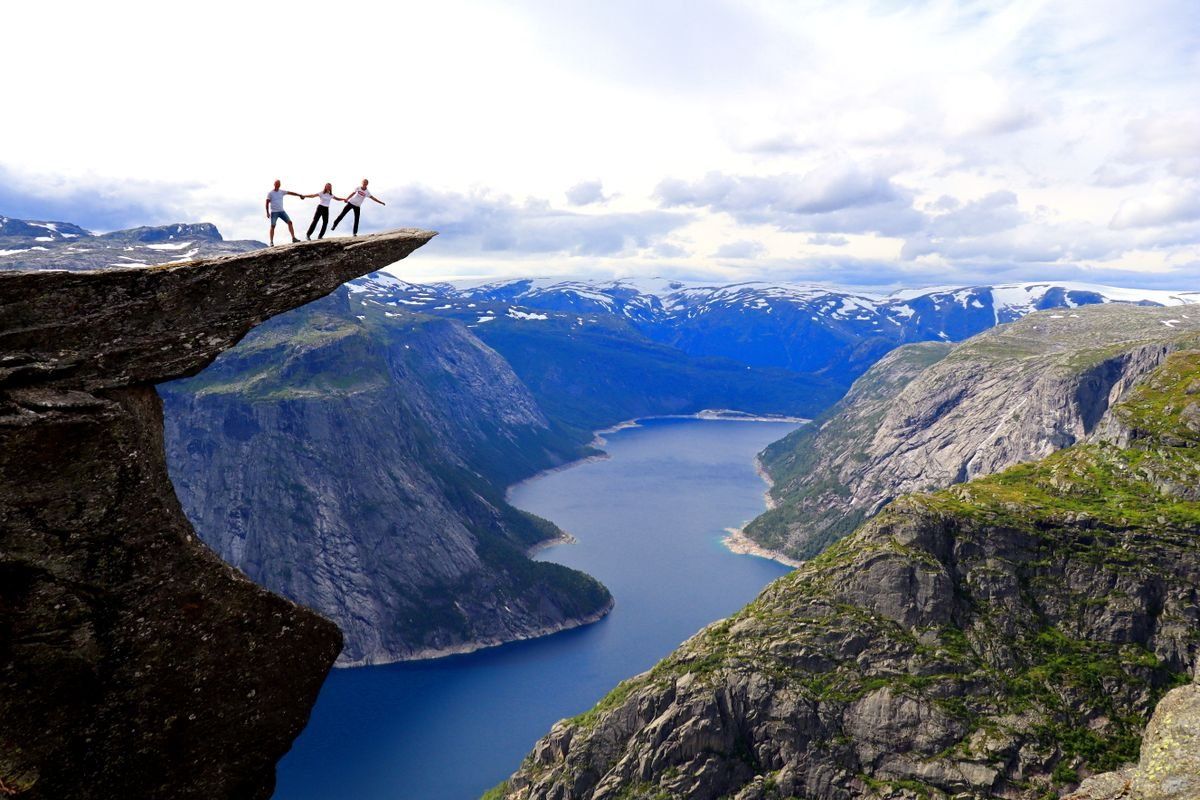 Three people standing on the edge of Trolltunga above a deep blue fjord