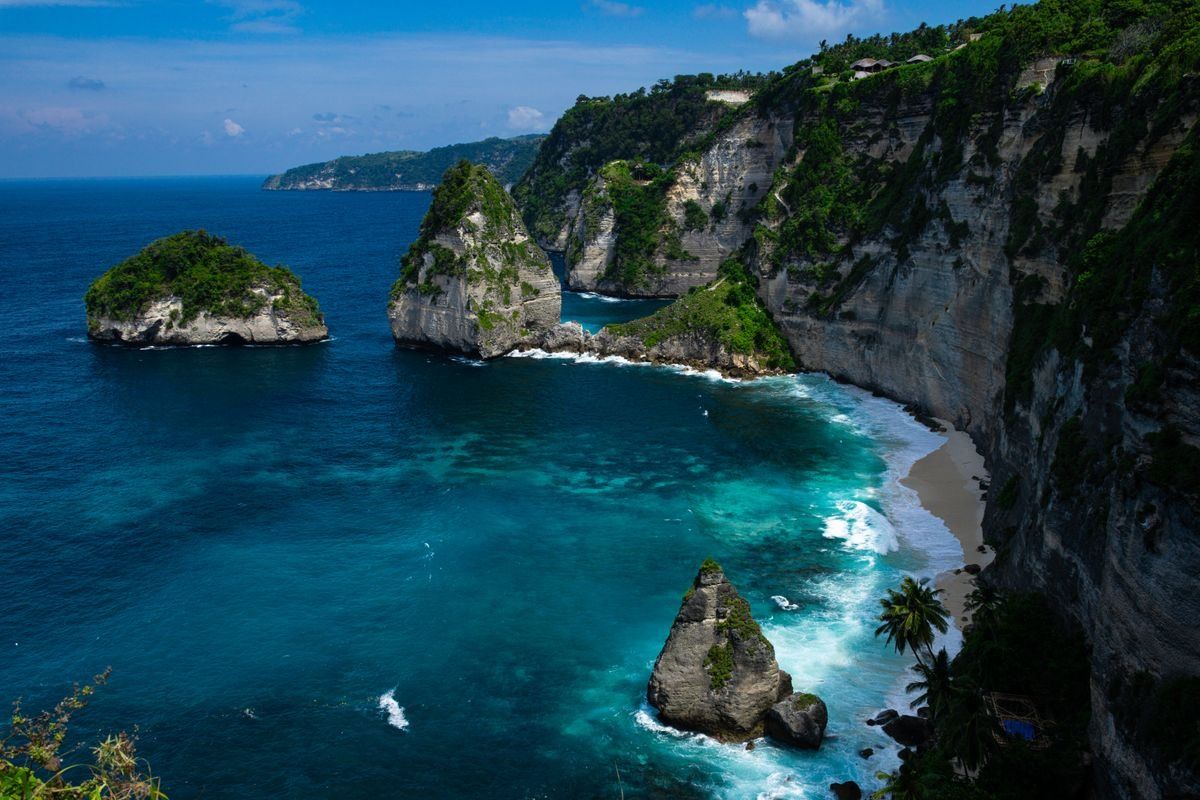 Towering coastal cliffs above a narrow beach and clear blue water on Nusa Penida