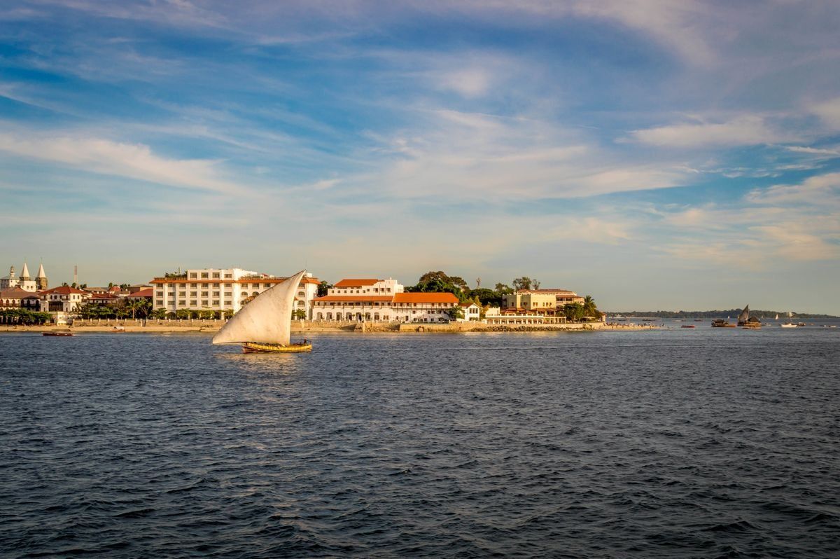 Traditional sailboat on calm water with Stone Town buildings along the shore