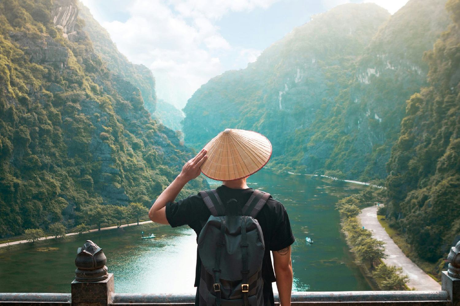 Traveler seen from behind wearing a conical hat looks out over the karst river valley of Trang An, Vietnam