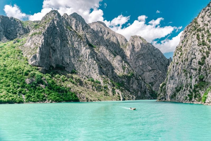 Small boat crossing a turquoise river winding through a steep rocky mountain gorge