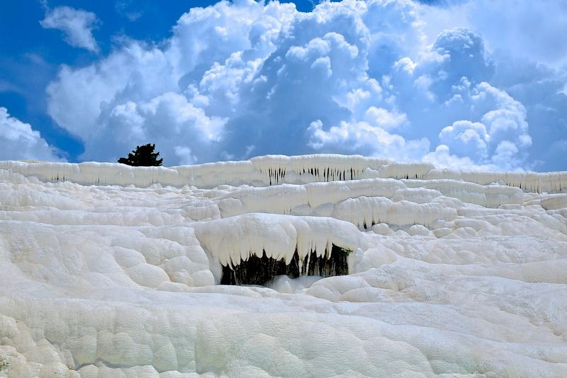 White limestone terraces of Pamukkale set against a dramatic cloudy sky with a lone tree