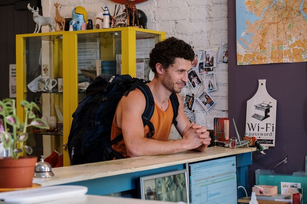 Backpacker leaning on a hostel reception desk with a large backpack