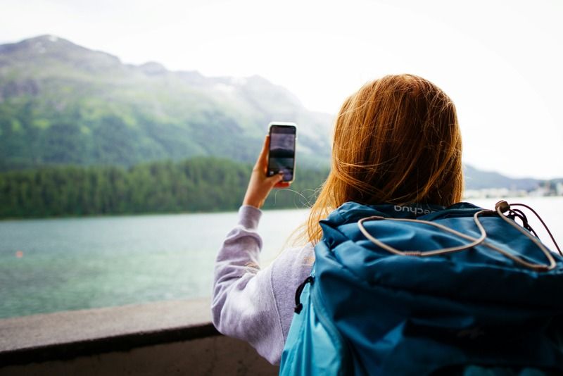 Backpacker taking a photo of a turquoise alpine lake surrounded by green mountains