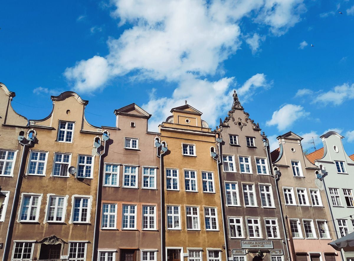 Colorful historic townhouses in Gdańsk beneath a bright blue sky with scattered clouds