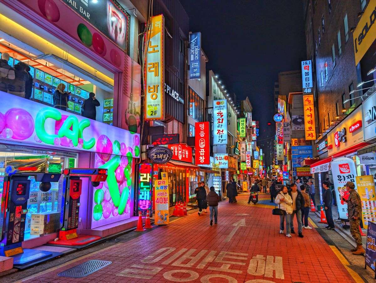 Colorful neon-lit street in Seoul at night with storefronts and scattered pedestrians