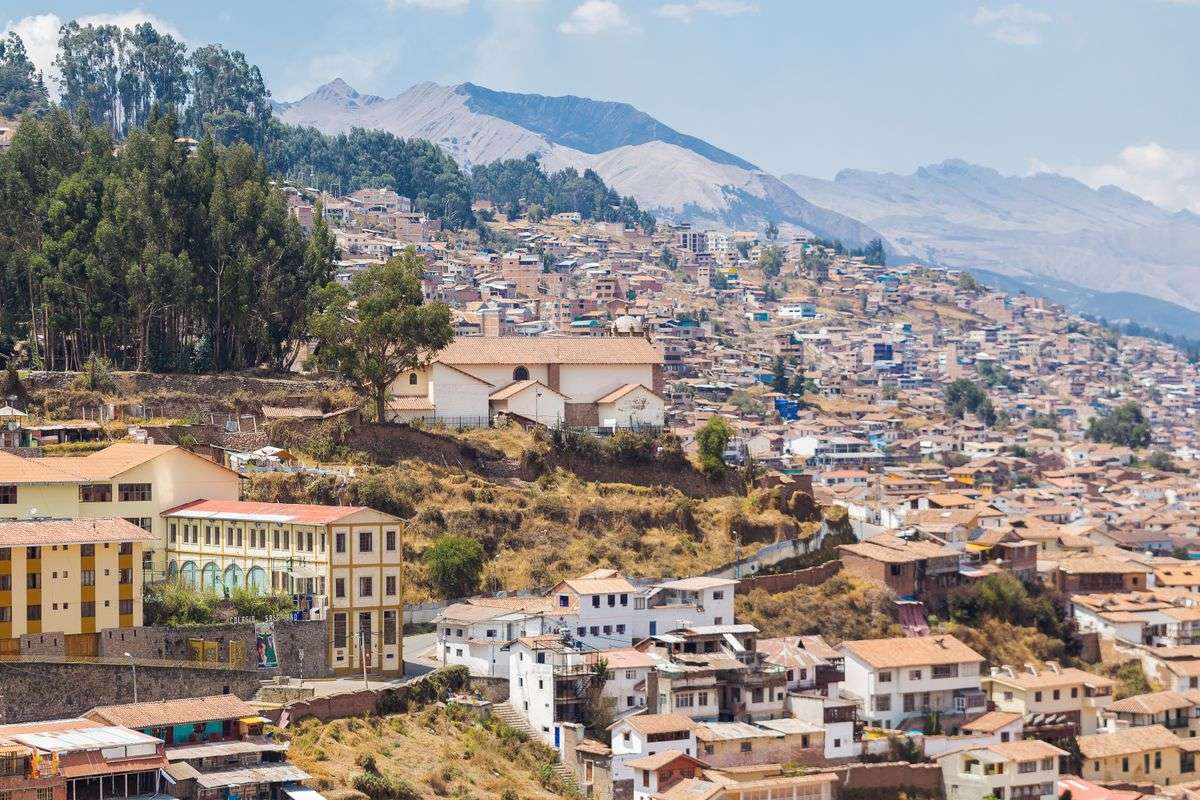 Cusco hillside neighborhood with dense houses, dry slopes, and mountains in the background