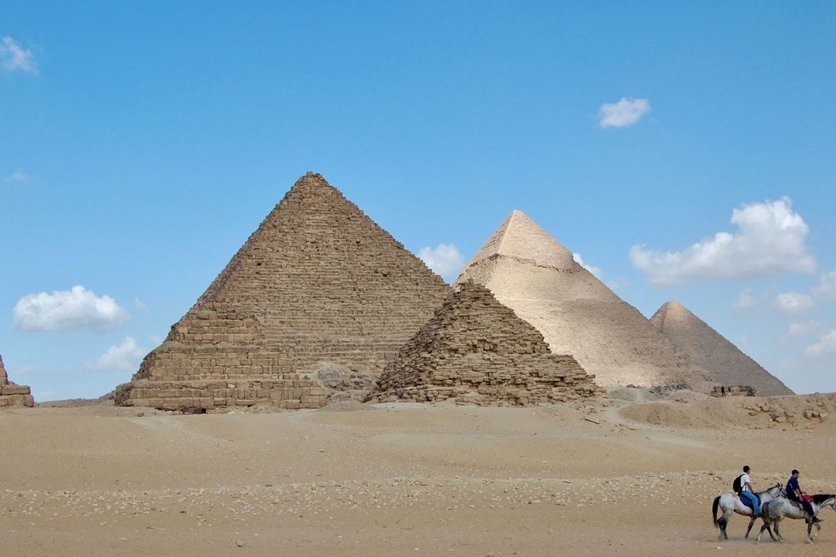 Giza pyramids in the desert with two riders on horseback under a bright blue sky