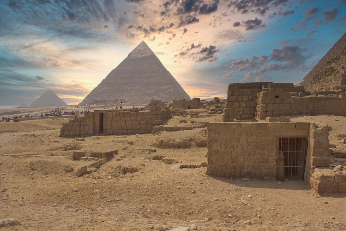 Giza pyramids at sunrise with stone ruins and a dramatic cloudy sky