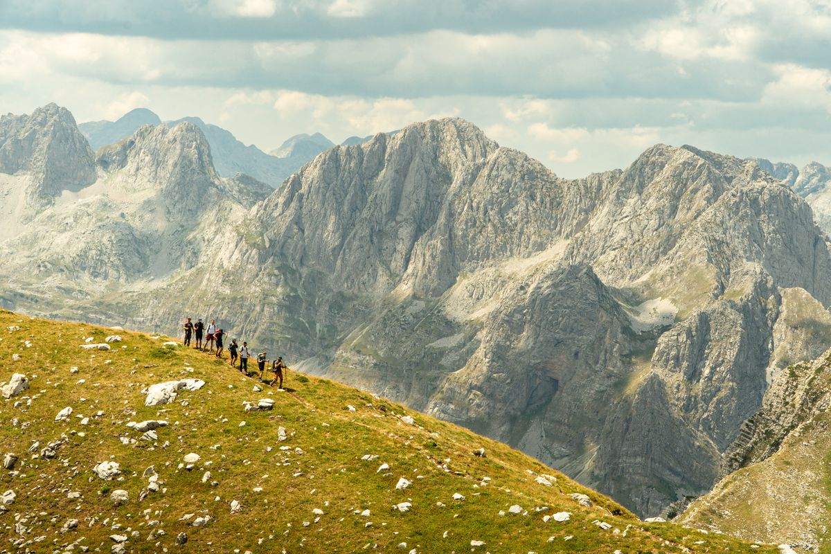Group of hikers crossing a grassy ridge with dramatic rocky mountains behind