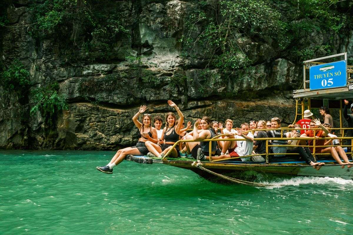 Group of travelers waving from a boat on turquoise water beside a rocky canyon wall