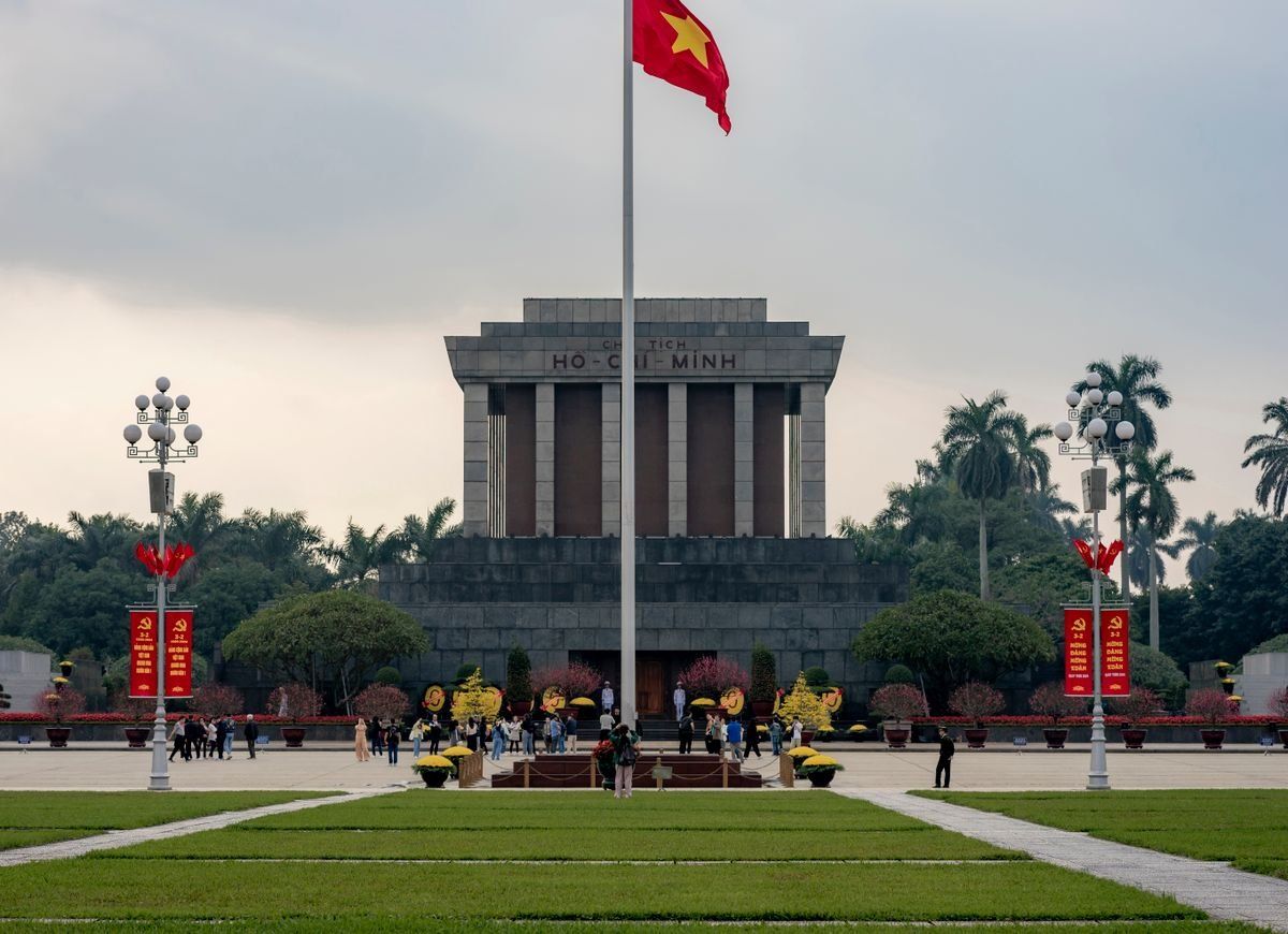 Ho Chi Minh Mausoleum with a tall Vietnamese flagpole and visitors in the square