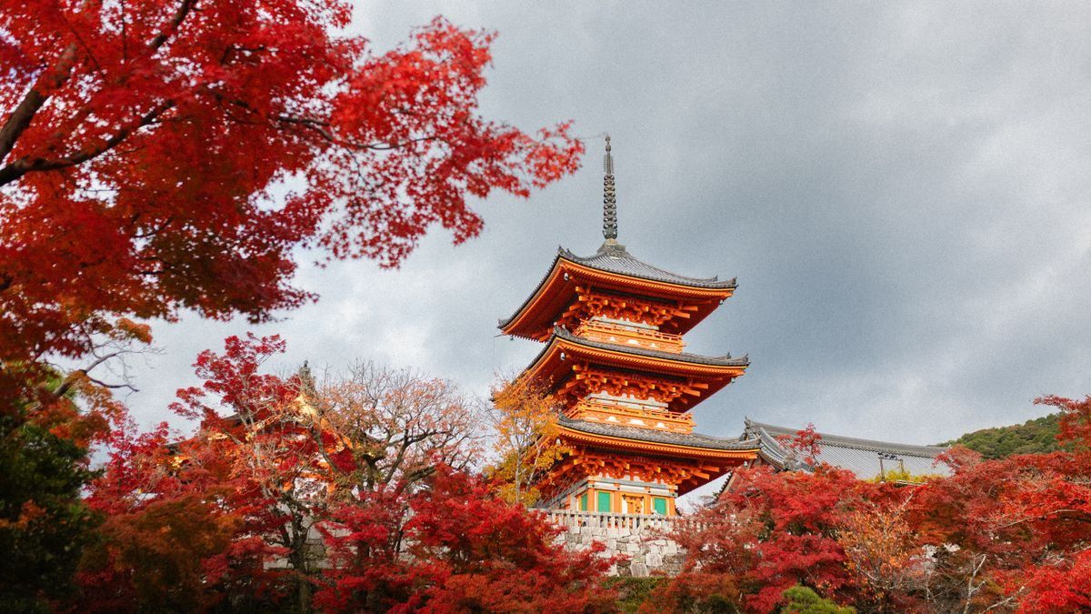Kiyomizu-dera pagoda framed by vivid red autumn leaves under a cloudy sky