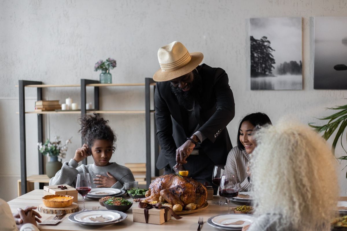 Man carving a roasted turkey at a dining table with family seated around it