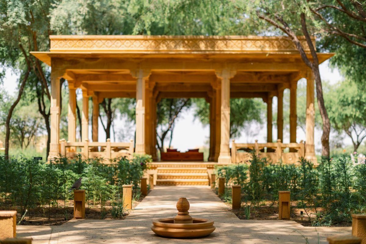 Open sandstone pavilion with columns and a central path surrounded by trees and low shrubs