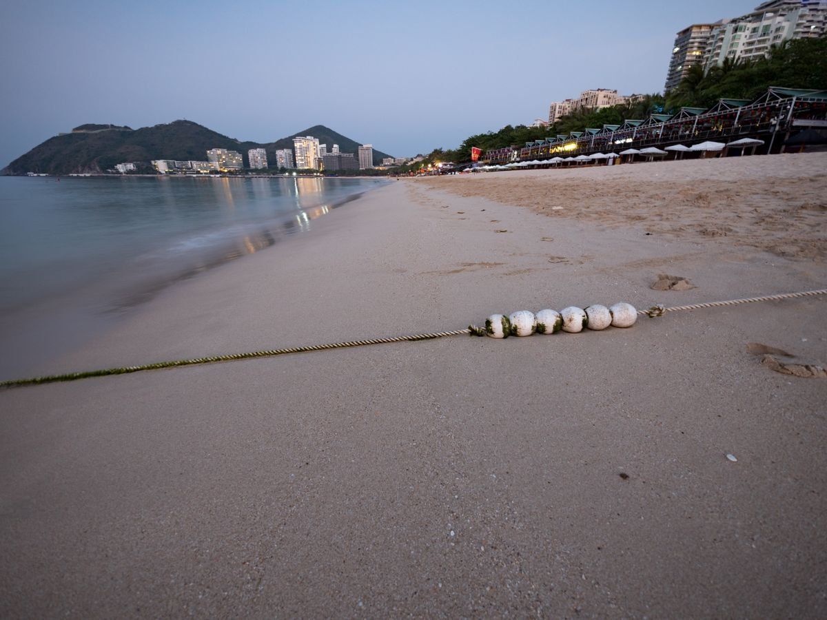 Quiet sandy beach at dusk with a rope line, calm water, distant hills and seaside buildings