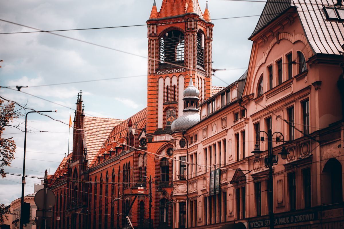 Red brick Gothic church tower and historic buildings along a street in Bydgoszcz
