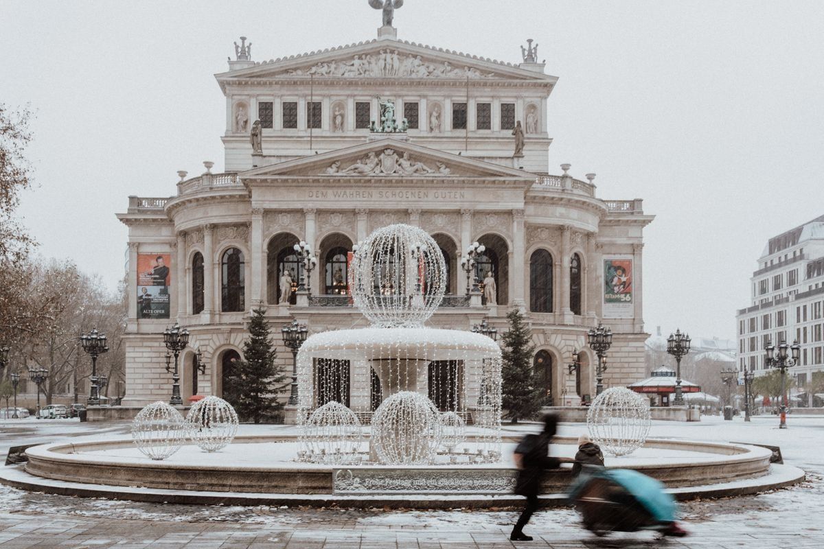 Snowy opera house square with illuminated fountain decorations and blurred pedestrians