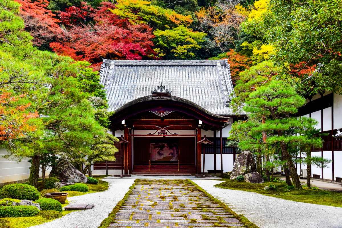 Traditional Japanese temple with a stone path and bright autumn trees in the garden