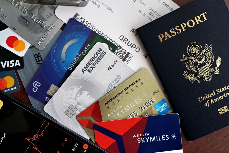 A flat lay of a US passport, boarding pass, and several credit cards arranged next to a phone showing a stock chart
