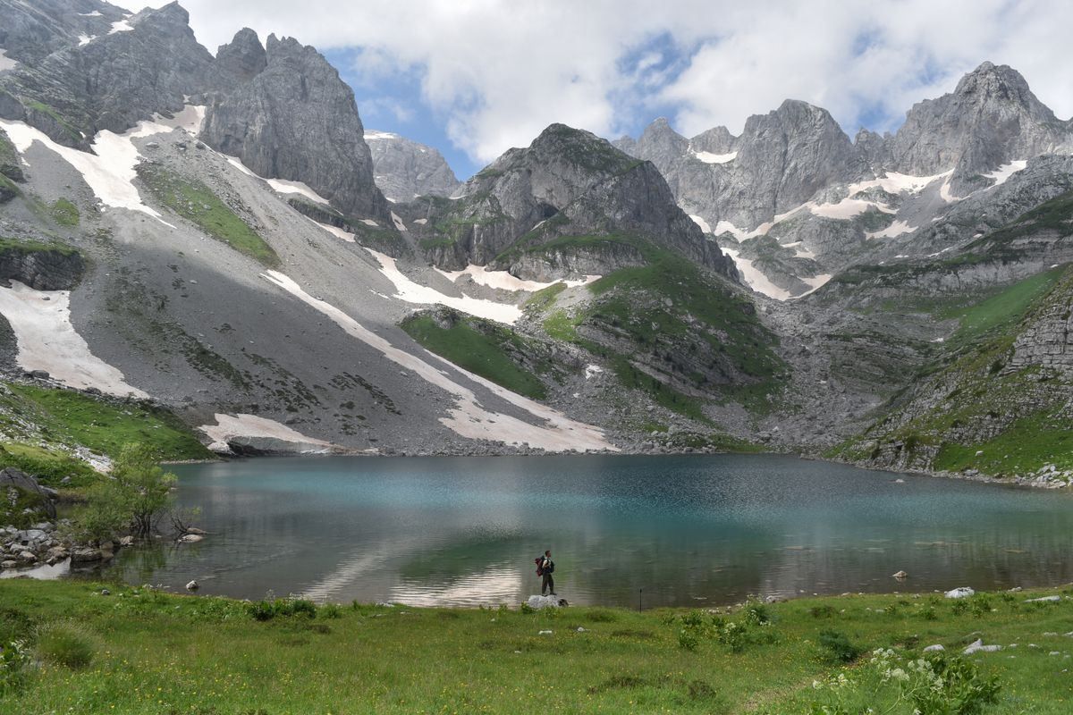 Turquoise mountain lake below jagged peaks with patches of snow on the slopes