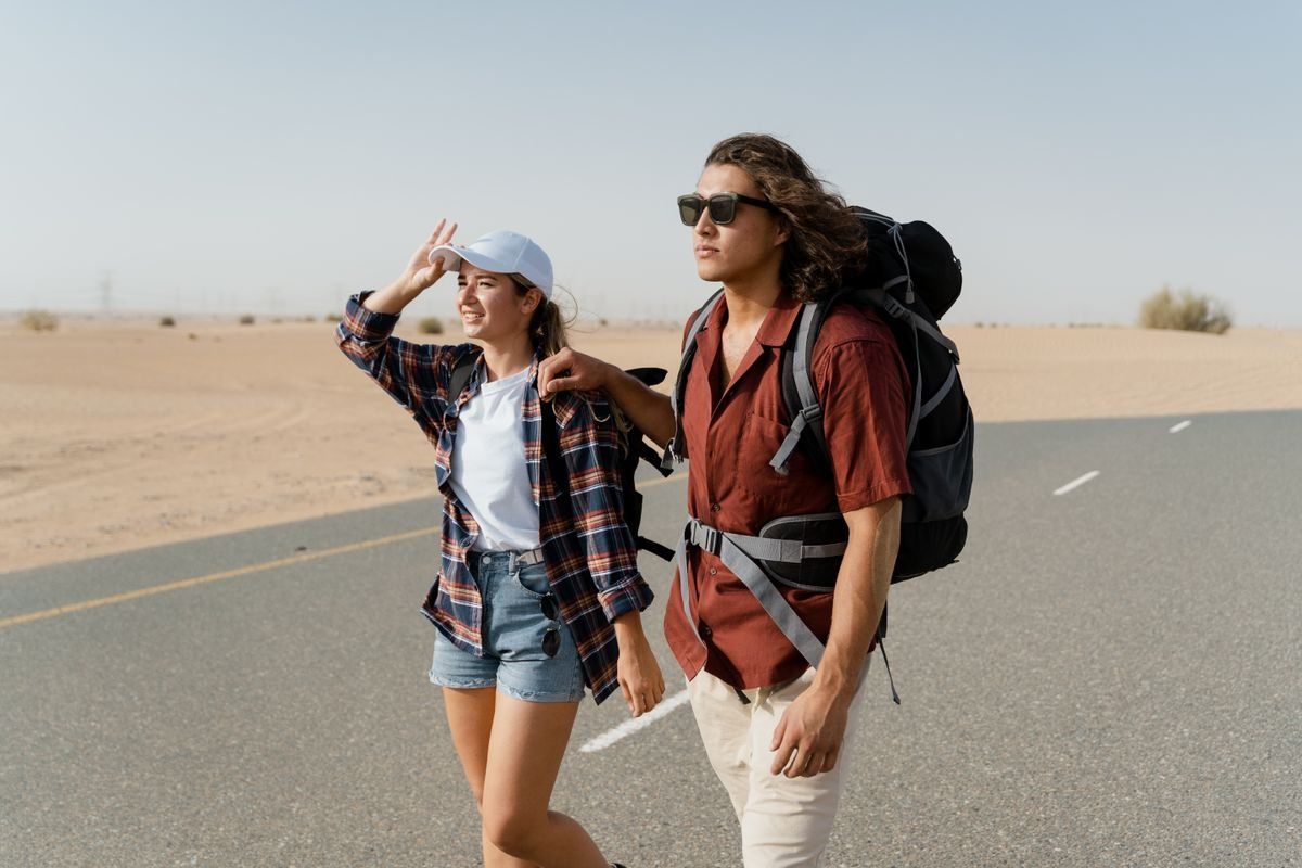 Two backpackers walking along a desert road under a clear sky