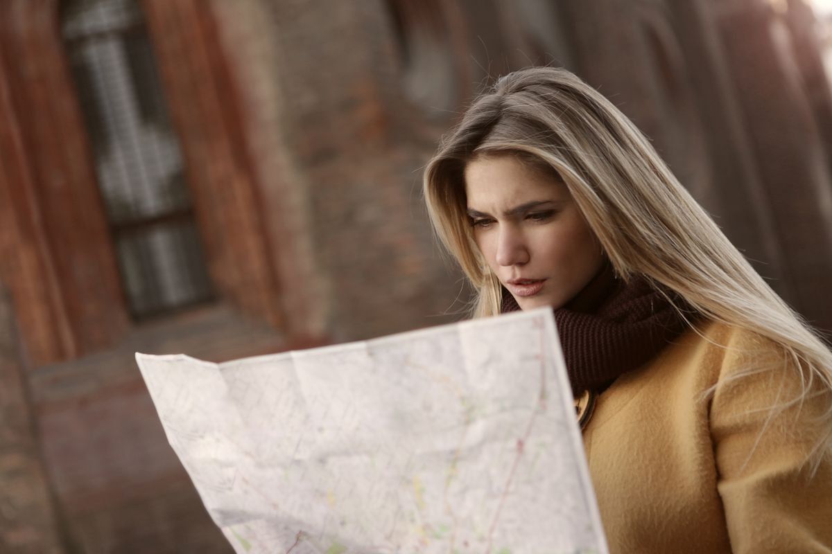 Woman in a brown coat studying a paper map outdoors