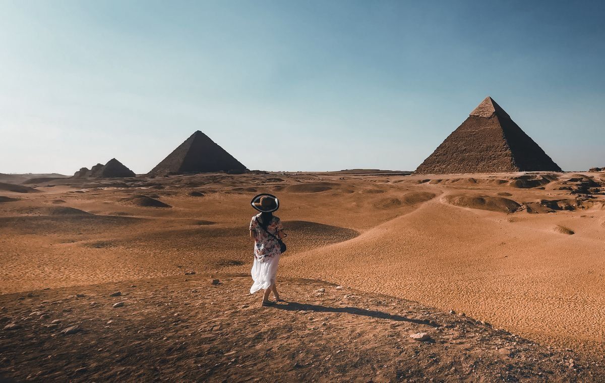 Woman walking across desert sand with the Giza pyramids in the distance