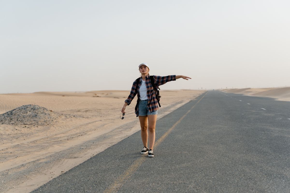 Young woman standing on an empty desert road with one arm extended