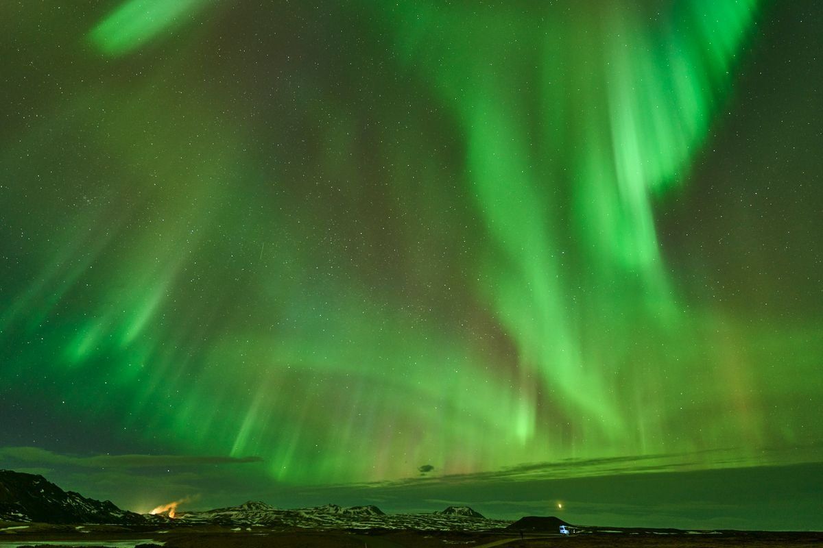 Bright green aurora sweeping across the night sky above a dark snowy landscape
