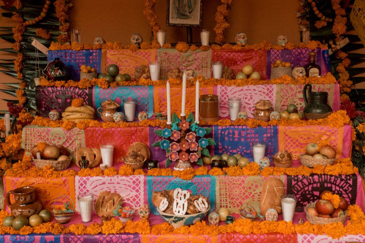 Colorful ofrenda altar with candles, marigolds, fruit, bread and papel picado