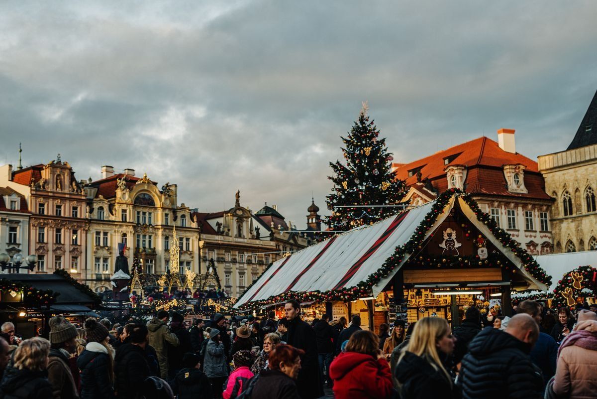 Crowded Christmas market with festive stalls and a lit tree in a historic city square