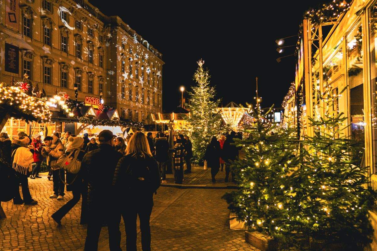 Crowded Christmas market street at night with lit stalls and decorated trees