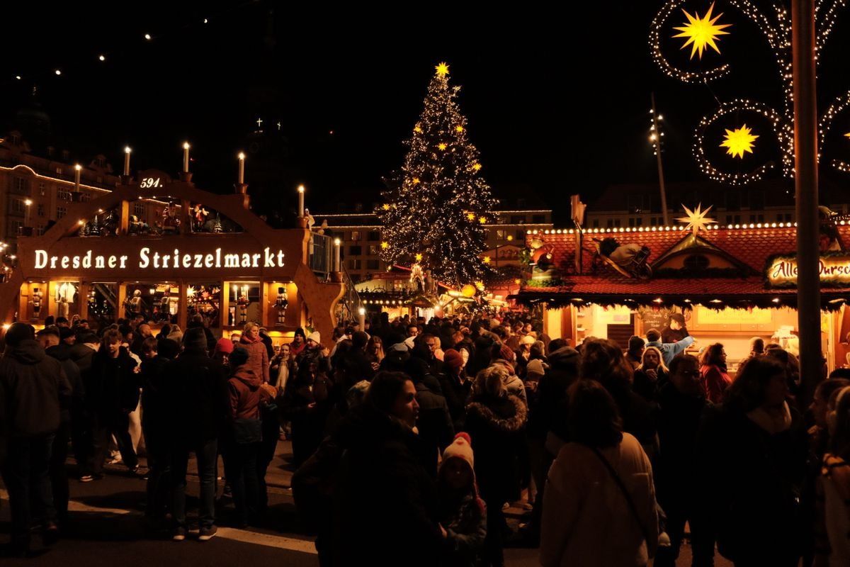 Crowded evening Christmas market with a lit tree and Dresden Striezelmarkt sign