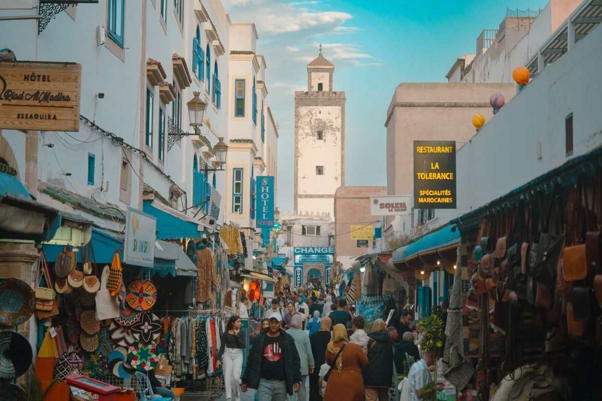 Crowded market street in Essaouira Medina lined with shops, signs and hanging goods