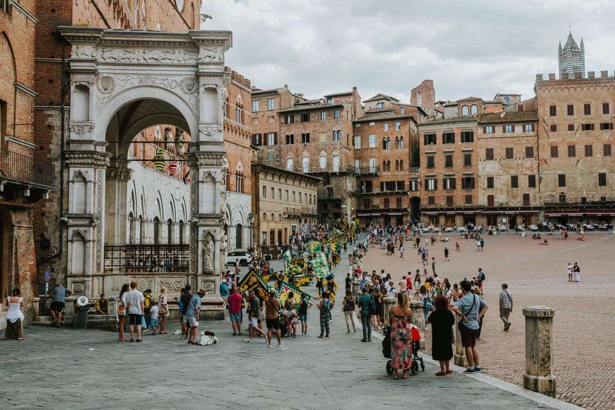 Crowds in Piazza del Campo in Siena beside an ornate arch and historic brick buildings