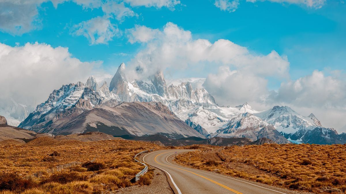 Curving road leading toward snow-covered Fitz Roy peaks under bright clouds